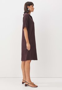 Kurzes lila Kleid mit Kragen und kurzen Ärmeln, das eine lockere Passform und einen leichten, strukturierten Stoff aufweist.