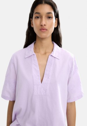 Lawendowa bluzka z kołnierzykiem, krótkimi rękawami i głębokim dekoltem w serek. Posiada kwiatowe hafty na rękawach oraz gładką teksturę.