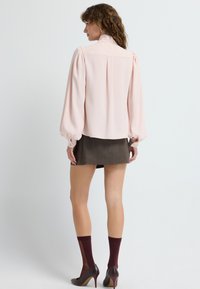 Blusa rosa con maniche a sbuffo, abbinata a una mini gonna grigia. La modella indossa calze borgogna e scarpe con il tacco a punta. Texture del tessuto liscia.