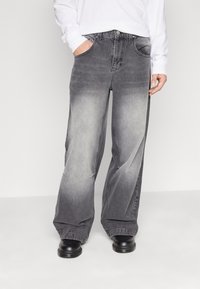 Sackiga grå jeans i denim med en blekt gradienteffekt, fem fickor och knäppning med knapp. Bärs med svarta skor.