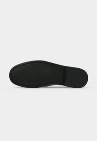 Semelle de chaussure habillée noire avec une légère texture et des coutures visibles le long des bords, présentée à plat sur un fond neutre.