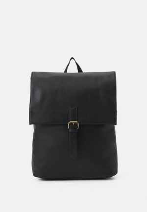 Schwarzer Leder-Rucksack mit Frontklappe, die durch einen goldfarbenen Schnallenriemen gesichert ist, und einer oberen Trageschlaufe vor einem einfarbigen Hintergrund.