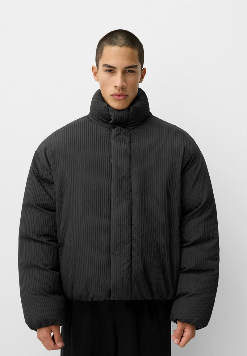 Schwarze Daunenjacke mit hohem Kragen, gerippter Textur und kurzer Passform. Verfügt über einen Knopfverschluss und weite Ärmel für zusätzliche Wärme.