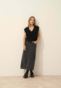 Svart ärmlös v-ringad stickad topp kombinerad med en lång mörkgrå denimkjol. Outfiten kompletteras med svarta snörskor.