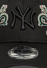 Svart caps med hevet, brodert New York Yankees-logo. Har intrikate grønne og røde dragebroderier på hver side. Justerbar stropp.