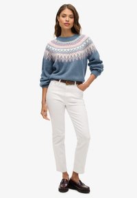 Blauer Pullover mit Fair-Isle-Muster in Pink und Weiß, kombiniert mit weißen Hosen und burgunderfarbenen Loafern. Stricktextur, lockere Passform.