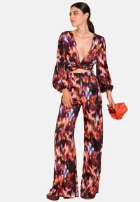 Conjunto floral colorido con un top de escote en V profundo y pantalones de pierna ancha. Hecho de tela suave. Los accesorios incluyen un bolso pequeño rojo.