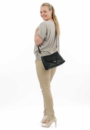 Schwarze Lederhandtasche mit abgerundeter Klappe, goldenen Beschlägen und einem langen Schultergurt. Helle graue Bluse und beige Hose sichtbar.
