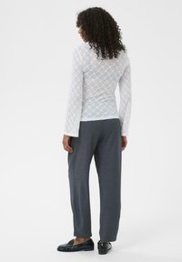 Hvid blonde langærmet top over grå høj talje bukser. Struktureret blomsterdesign på toppen, glat stof, kombineret med sorte loafers.