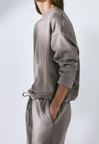 Grijze pullover met een ontspannen pasvorm, ronde hals en lange mouwen, gecombineerd met bijpassende grijze joggers, gemaakt van zacht materiaal.