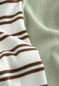 Gros plan de tissu côtelé avec des rayures horizontales marron et blanches à côté d’un tissu côtelé vert clair uni.