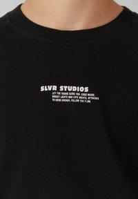 Zwarte katoenen sweatshirt met ronde hals en witte bedrukte merktekst. De tekst bevat de naam "SLVR STUDIOS" en een slogan.