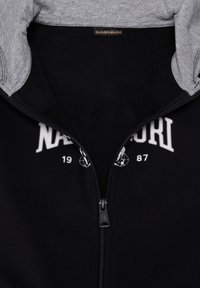 Felpa nera con zip e cappuccio grigio. Presenta scritte bianche e dettagli numerici, una consistenza morbida e una zip liscia.