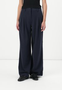 Navy wide-leg trousers with pleats, crafted from a soft fabric. High waist design, side pockets, and a smooth texture. Paired with black shoes.