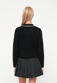 Melna adīta kardigāna ar pieguļošu formu, ar baltu akcentu apkakli un garām piedurknēm, kombinēta ar plīšu pelēku svārku.