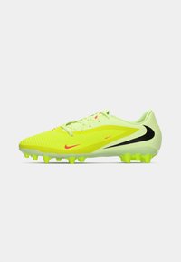 Jaskrawożółte i zielone korki piłkarskie Nike z neonowymi wkrętami, czarnym logo Swoosh i sznurowadłami, przedstawione w profilu bocznym na białym tle.