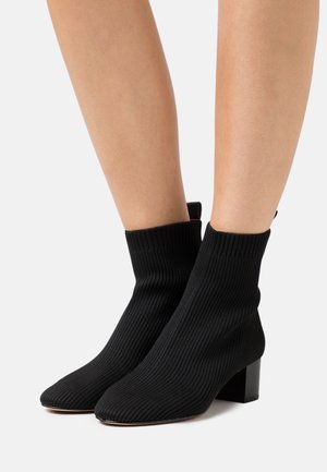 Stivaletti neri a coste con punta affusolata e tacco alto spesso. Il materiale lavorato a maglia si estende oltre la caviglia per un look aderente.