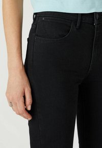 Czarne dżinsy w dopasowanym kroju, z klasycznym pięciopakowym wzorem, widocznymi ściegami i gładką teksturą.