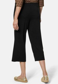 Pantalons noirs courts avec une coupe décontractée et une taille élastique, présentant une texture lisse et une coupe droite. Chaussures dorées à enfiler.