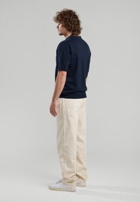 Navy lyhythihainen polo-paita yhdistettynä vaaleanruskeisiin väljiin housuihin ja valkoisiin tennareihin, joissa on yksinkertainen muotoilu ja pehmeä rakenne.