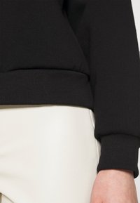 Svart sweatshirt med ribbade ärmar och nederkant, med en mjuk textur. I kombination med åtsittande vita byxor, som visar en sömlös design.