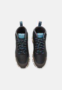Zapatillas altas negras con una parte superior texturizada, cordones azules y una suela de color crema; incluye un logotipo y una lengüeta en el talón.