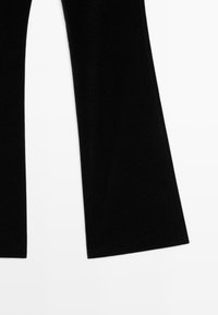 Pantalons évasés en velours noir avec une texture lisse, dotés de coutures sur les côtés et d'une coupe large pour un ajustement décontracté.