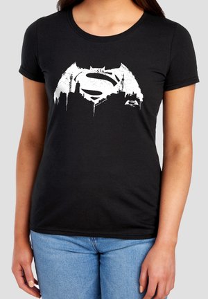 Black t-shirt with white Batman and Superman combined logo above city skyline graphic worn by person in blue jeans.