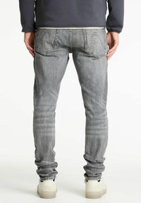 Jeans de mezclilla grises con un ajuste slim, que presentan bolsillos traseros, un ligero desvanecimiento y una pierna cónica. Combinados con zapatillas de color claro.