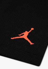 Μαύρο διχτυωτό ύφασμα με εμφανές πορτοκαλί λογότυπο Jumpman, που απεικονίζει τη σιλουέτα ενός παίκτη μπάσκετ στον αέρα.