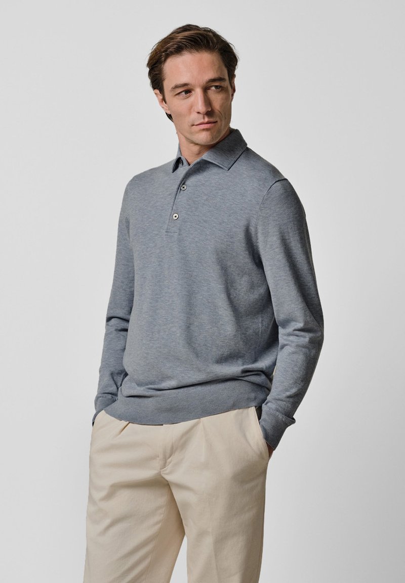 Grau langärmeliges Poloshirt mit Kragen und Knopfleiste. Der Pullover hat eine glatte Textur und wird durch hellbeige Hosen ergänzt.