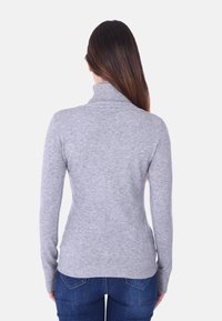 Maglione grigio a collo alto in maglia con una forma aderente, maniche lunghe e texture a coste sul colletto e sull'orlo. Indossato con jeans blu.