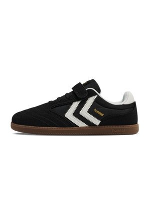 Sort sneaker med hvide chevron-striber, brun sål, hvid hællap og velcrolukning, mærket "hummel" på siden og sålen.