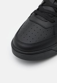 Sneaker in pelle nera con una texture liscia, tomaia perforata e suola nera piatta. Progettato con lacci neri e dettagli di cucitura rinforzati.