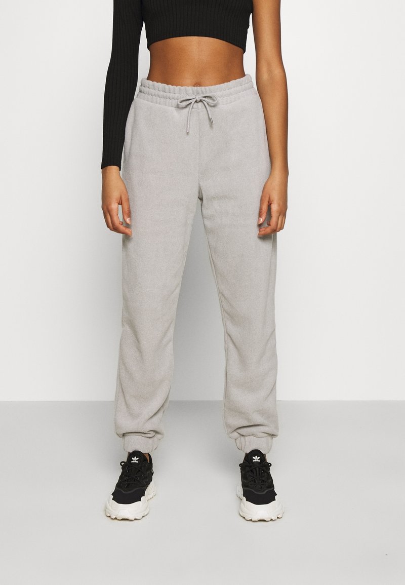 Hellgraue Fleece-Jogginghosen mit elastischem Bund und Kordelzug, ausgestattet mit elastischen Bündchen an den Knöcheln, kombiniert mit schwarzen Sportsneakern.
