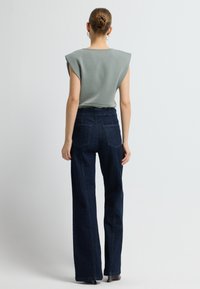 Světle zelený top s krátkým rukávem a vycpanými ramenními ploškami, kombinovaný s tmavě modrými flared džínami s vysokým pasem, které mají zadní kapsy a jemné švy.