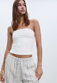 Bílý elastický top bez rukávů vyrobený z měkké látky, zkombinovaný s světle šedými, pruhovanými kalhotami volného střihu s elastickým pasem.