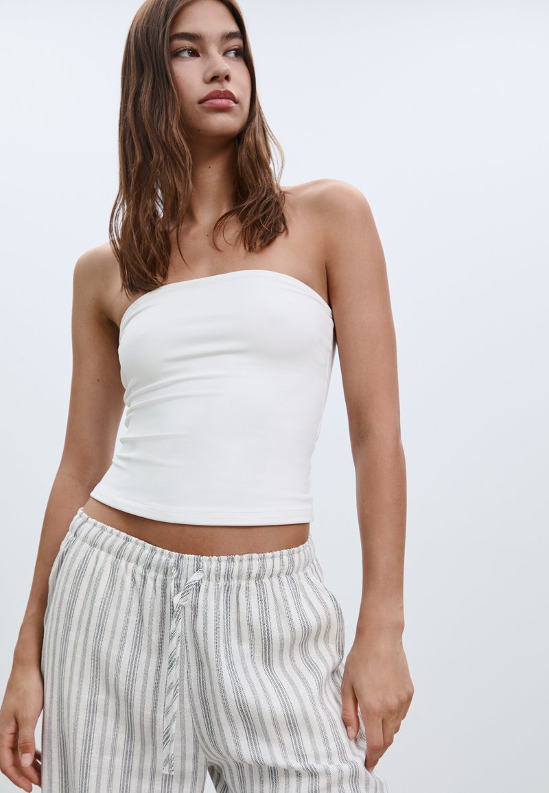 Bílý elastický top bez rukávů vyrobený z měkké látky, zkombinovaný s světle šedými, pruhovanými kalhotami volného střihu s elastickým pasem.