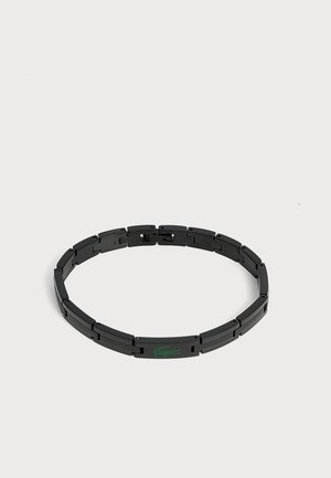 Bracelet à maillons en métal noir avec un logo crocodile vert sur un maillon rectangulaire sur fond blanc.