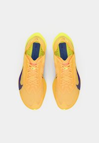 Une paire de chaussures de course Nike vives orange et jaune avec des logos swoosh violets, vues d'en haut sur un fond blanc.