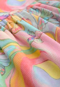 Soft, ribbed fabric with pastel floral and butterfly patterns in pink, yellow, green, and blue hues, showing gentle folds and texture.
