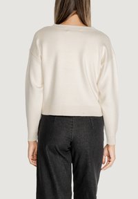 Pullover crema, corto, con scollatura ampia, maniche raglan e orlo a coste. Abbinato a pantaloni a vita alta di colore grigio scuro.