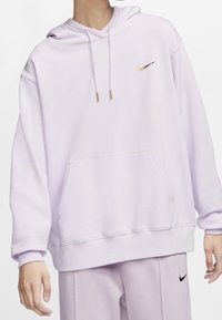 Lila huvtröja i mjukt tyg, med en framficka och en guldfärgad Nike-logotyp på vänster bröst. Dragsnören med gyllene ändar.