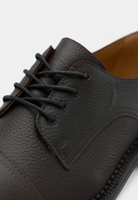 Shoe de vestido em pele castanha com uma superfície texturizada, com atacadores pretos e detalhes de costura subtis ao longo das bordas.