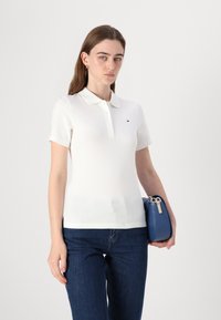 Valge polo särk lühikeste varrukatega, nööpide rida ja väike logo. Koos tumedate siniste teksade ja sinise käekotiga. Sile tekstuur.