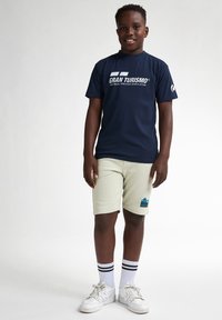 Marineblauwe katoenen T-shirt met witte "Gran Turismo" tekst, gecombineerd met lichtgroene shorts met een meerkleurig palmbomenlogo en gestreepte sokken.