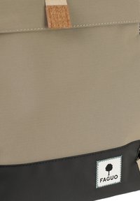 Borsa in tessuto beige e nera con etichetta cucita che mostra un simbolo ad albero e il nome del marchio "FAGUO" vicino al bordo inferiore.
