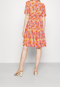 Blumendruckkleid in lebhaften Farbtönen von Pink, Orange und Gelb, mit geraffter Taille, kurzen Ärmeln und einem gestuften Rock.