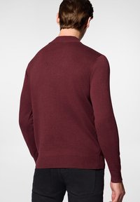 Burgundowa sweter z długimi rękawami, okrągłym dekoltem, żeberkowymi mankietami i dołem; wykonany z miękkiego, teksturowanego materiału, eksponowany z tyłu.