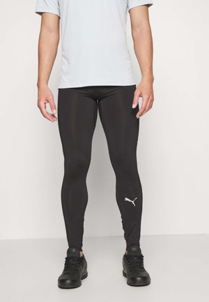 Czerną sportowe legginsy wykonane z elastycznego materiału, o dopasowanym kroju, matowym wykończeniu i białym logo Pumy na dolnej części lewej nogawki.